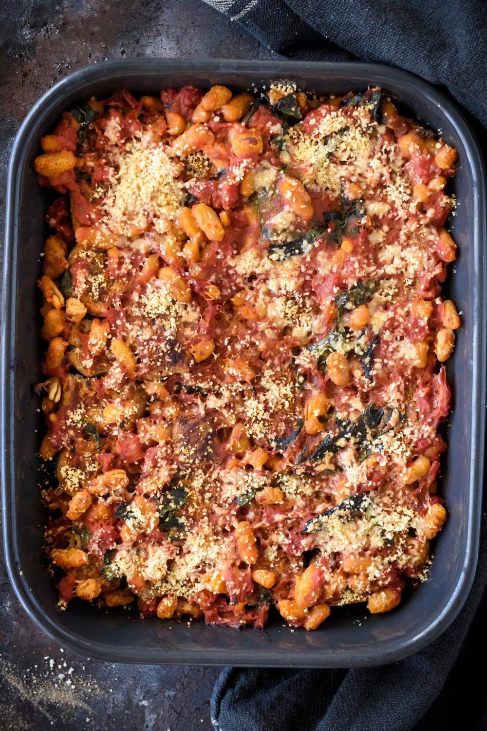 A baking dish filled with tomato and bean casserole covered in parmesan cheese.