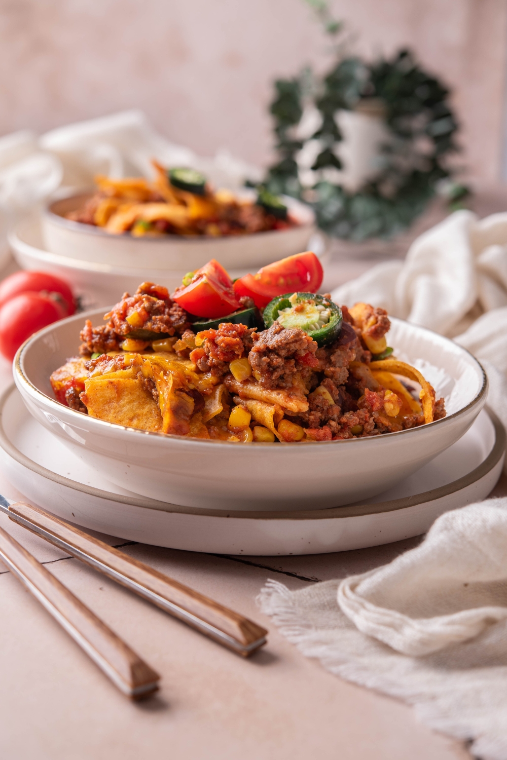 A bowl of Frito taco casserole topped with melted cheese, diced tomatoes, and sliced jalapeños.