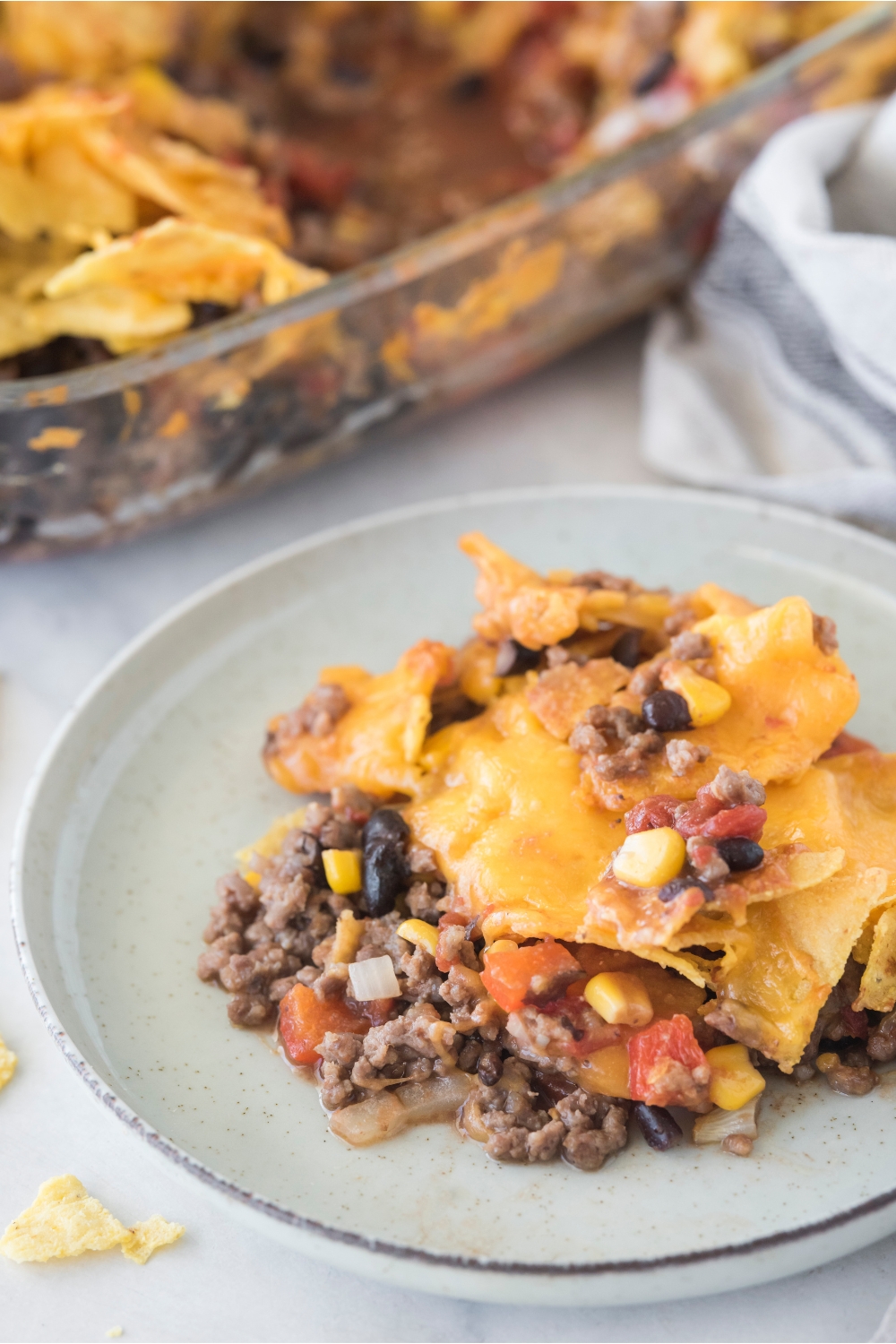 A serving of Tex-Mex casserole piled high on a plate with the rest of the casserole in the background.