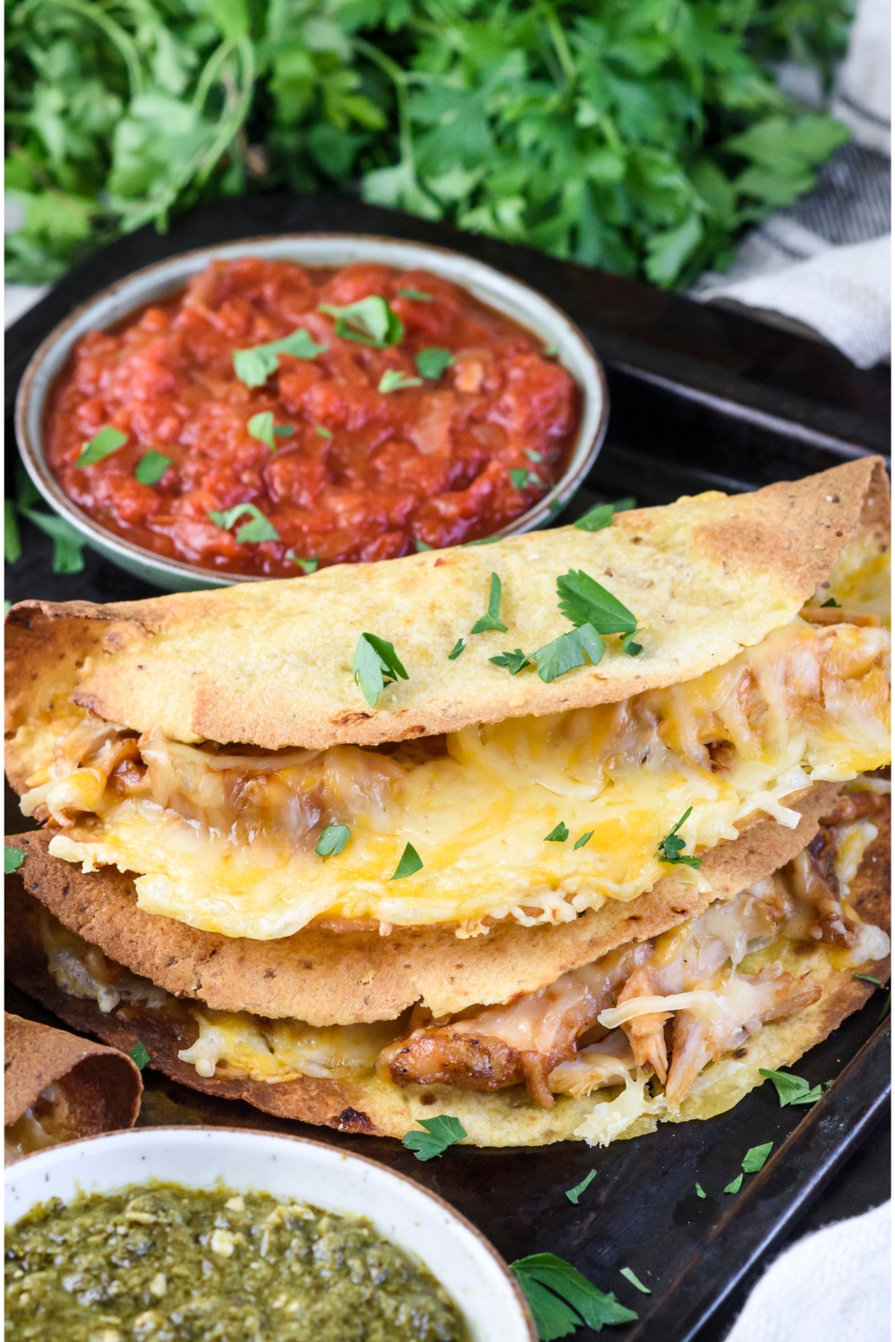 Two crispy tacos stacked on top of each other on a tray with bowls of red and green salsa. Both tacos are filled with cooked and shredded chicken and melted cheese.