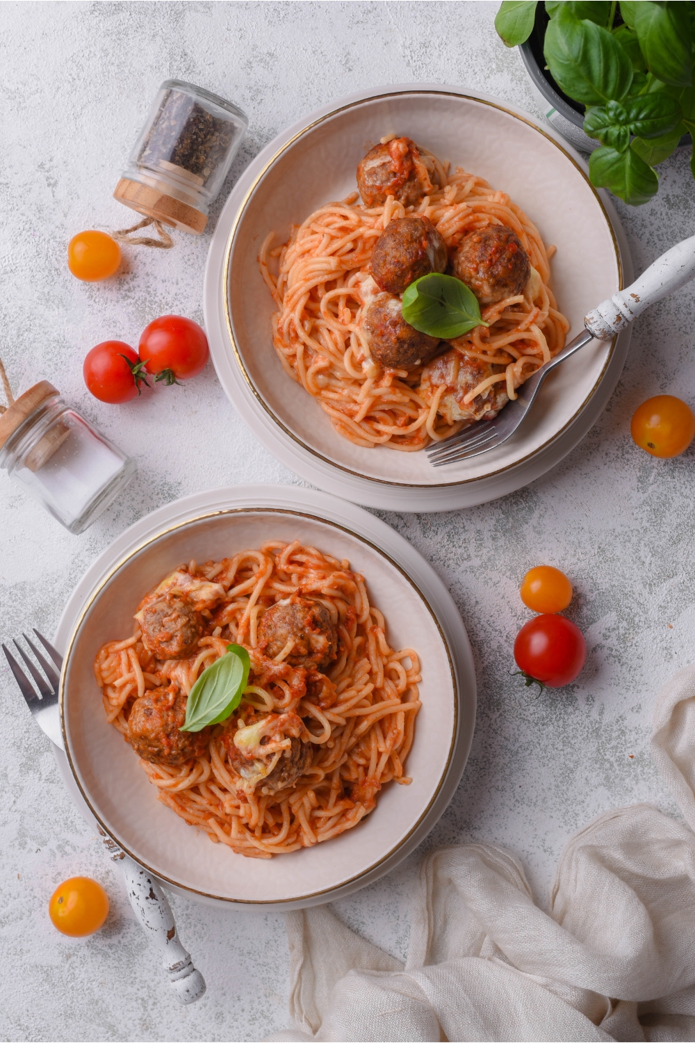 Two bowls of spaghetti in red sauce, each topped with meatballs and a garnish of fresh basil.