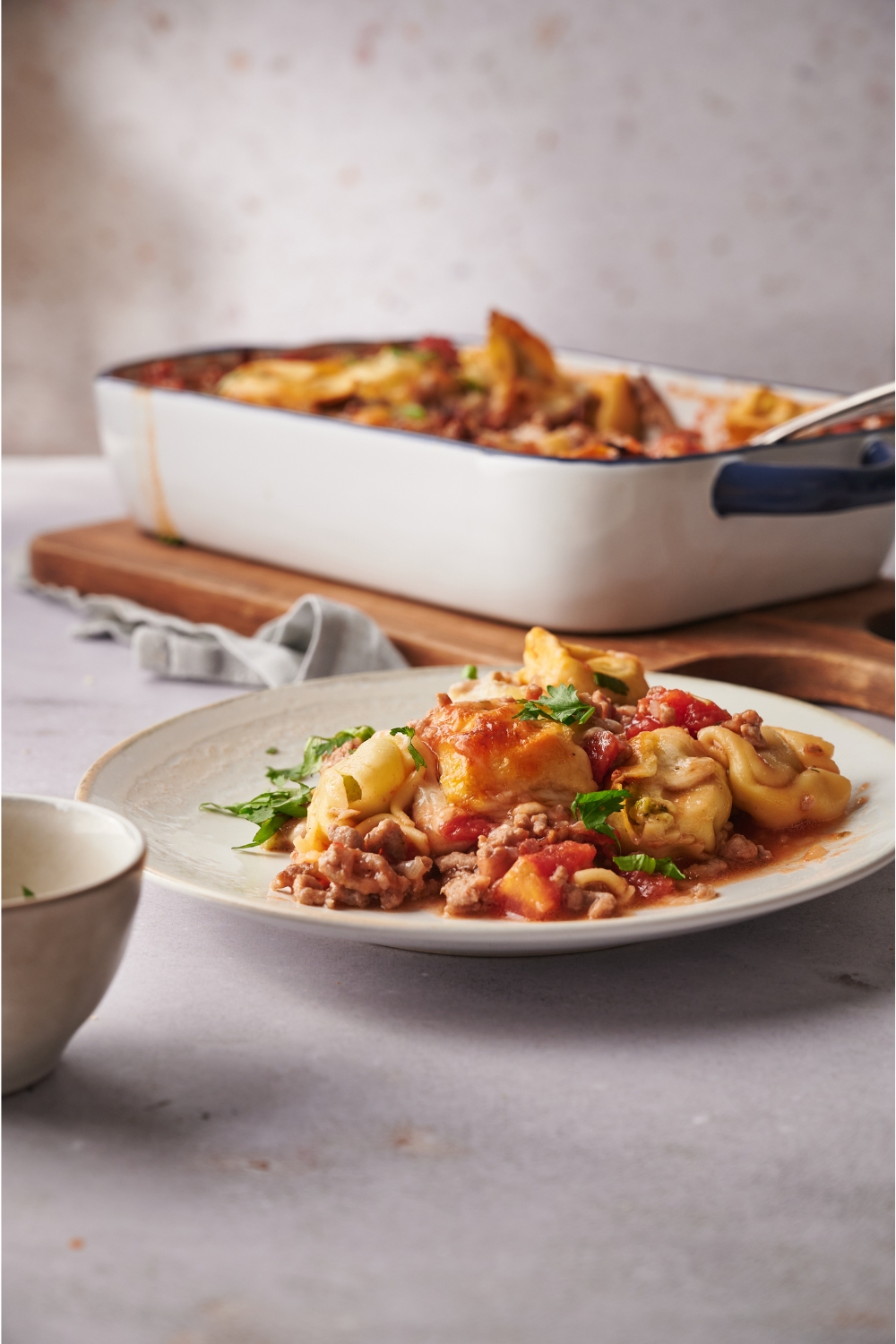 A serving of tortellini casserole with chunks of ground beef, cooked tomatoes, melted cheese, and fresh herbs.