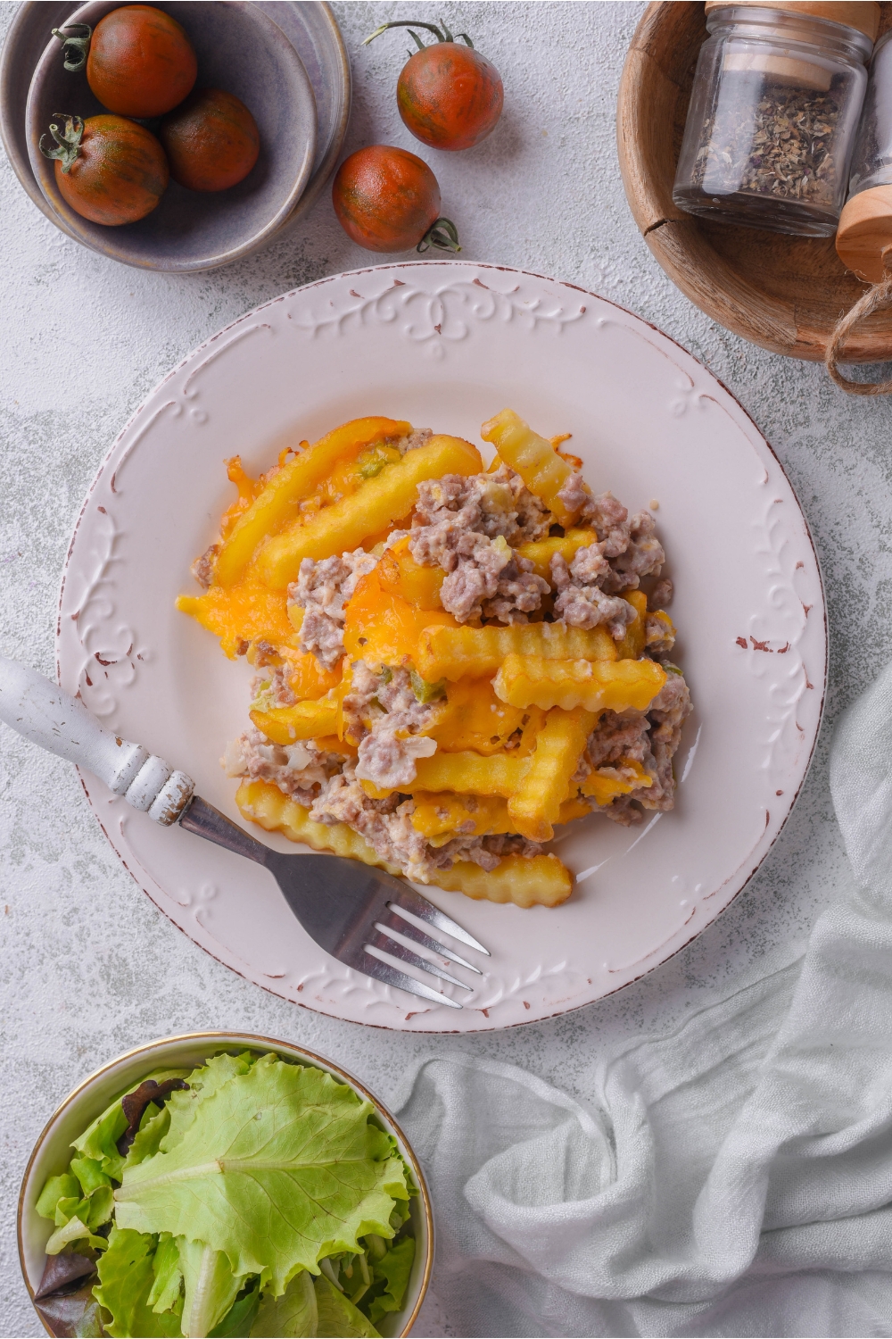 Overhead view of a serving of french fry casserole covered in melted cheese with a fork on the plate next to it.