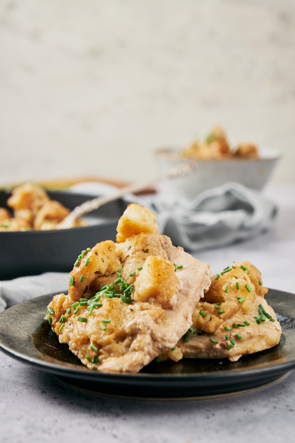 Two pork chops stacked on each other and each is covered in a creamy sauce with stuffing and a garnish of chopped chives.