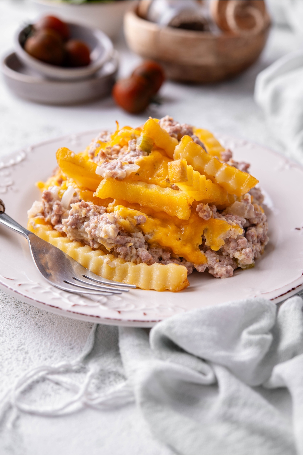 A serving of french fry casserole on a plate piled high with a fork on the plate.