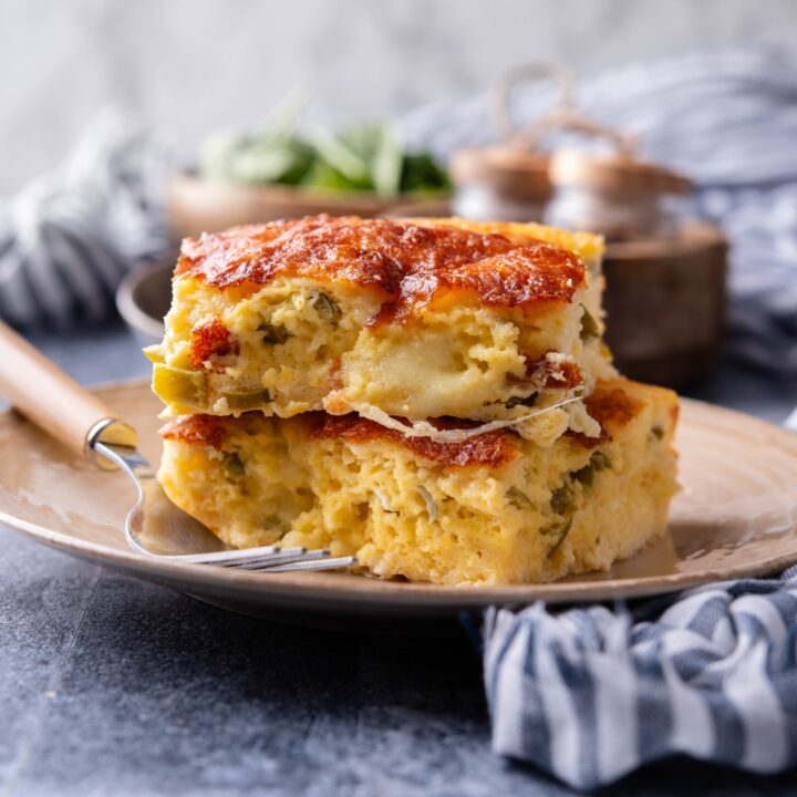 Two square servings of green chili egg casserole stacked on top of each other with a fork on the plate.