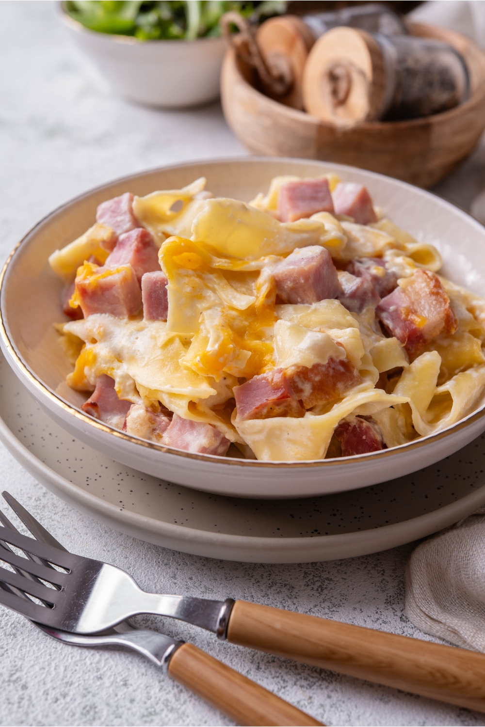 A bowl of ham and noodle casserole atop a plate with two forks next to it.