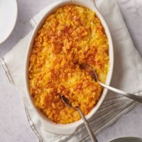 A casserole dish with baked hashbrown casserole and two serving spoons in it.