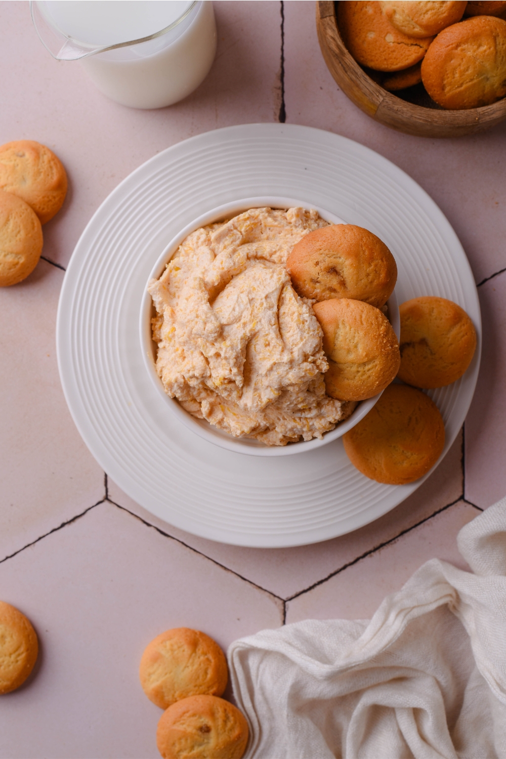 Pumpkin cream cheese dip in a white ramekin with two vanilla wafers sticking out of the dip and two more cookies next to the ramekin.