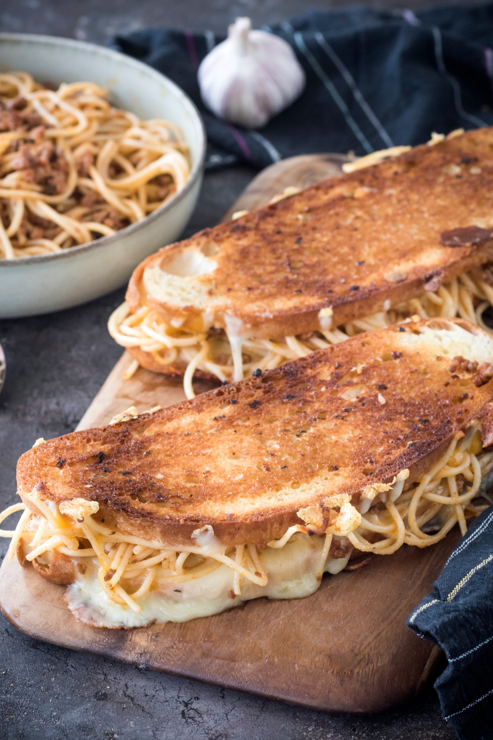 Two spaghetti sandwiches on toasted bread with melted cheese and noodles spilling out of the sides.