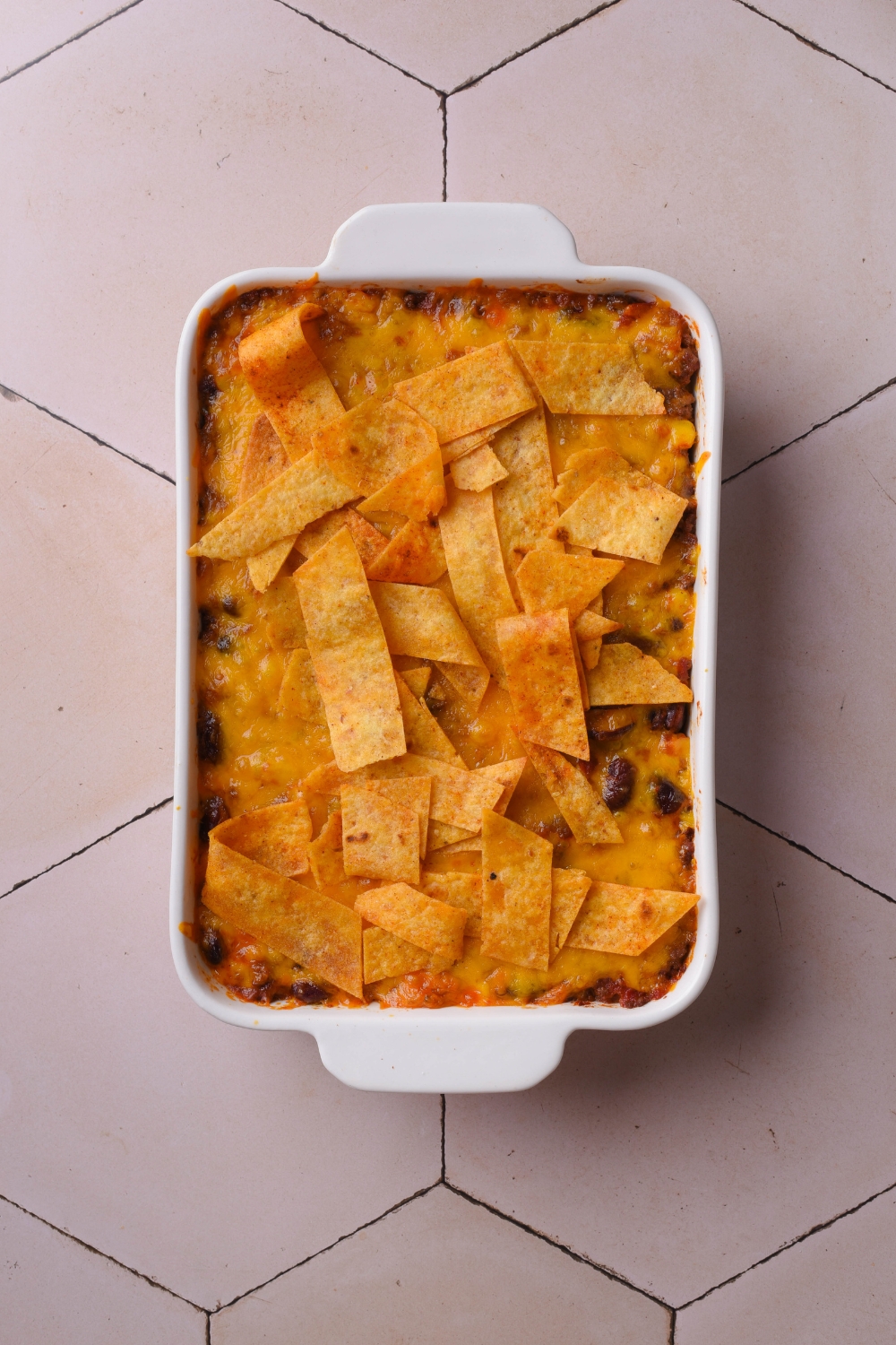 A baking dish filled with freshly baked casserole covered in melted cheese and topped with corn chips.