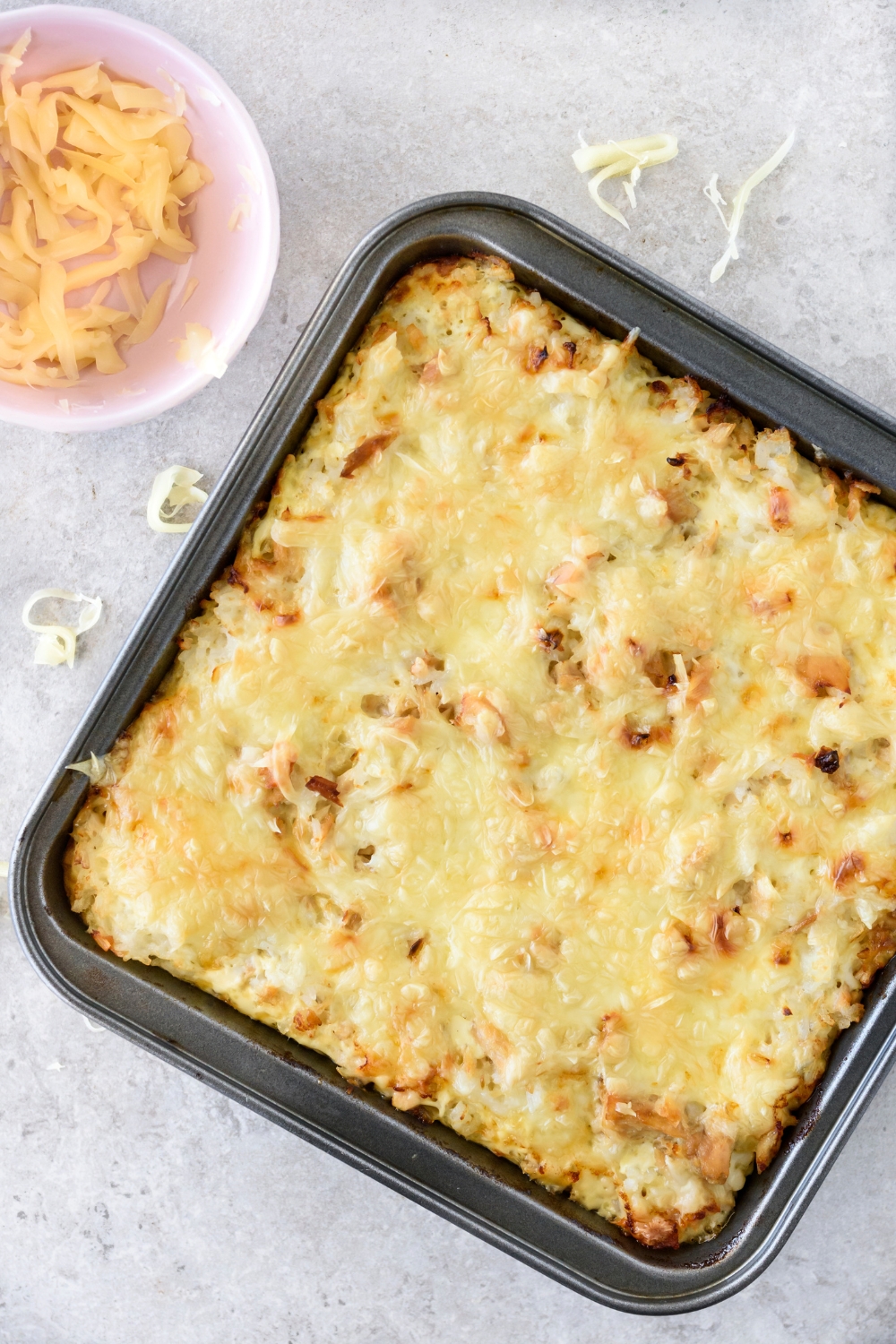 A square baking dish filled with baked tuna rice casserole covered in melted cheese.