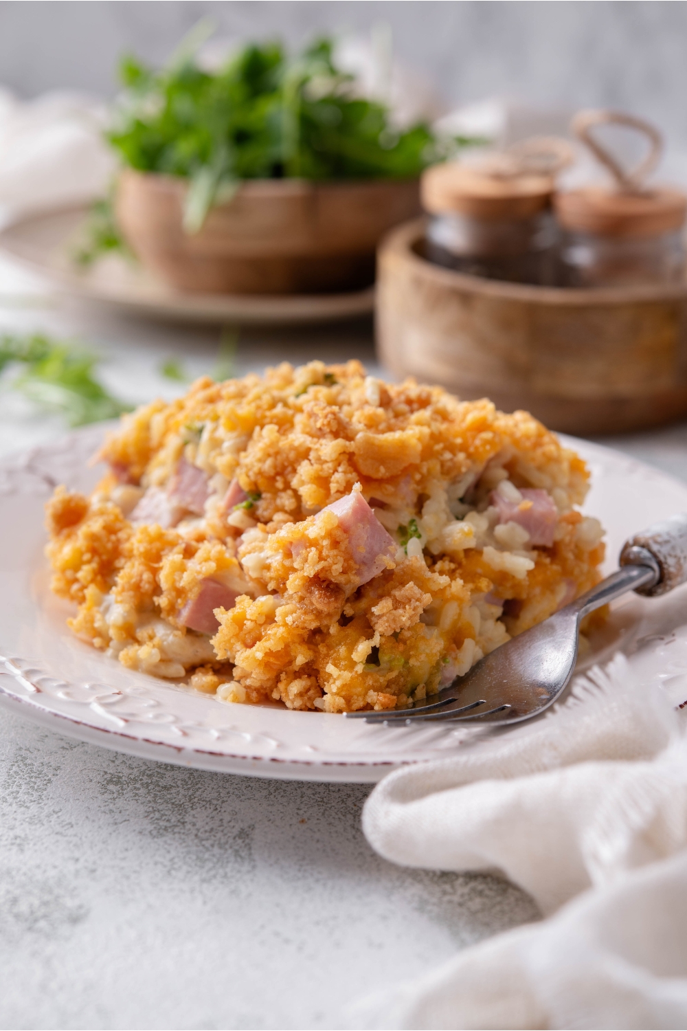 A serving of ham casserole covered in crushed crackers and melted cheese with a fork on the plate.