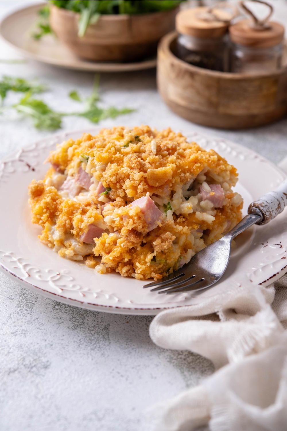A serving of ham casserole covered in crushed crackers and melted cheese with a fork on the plate.