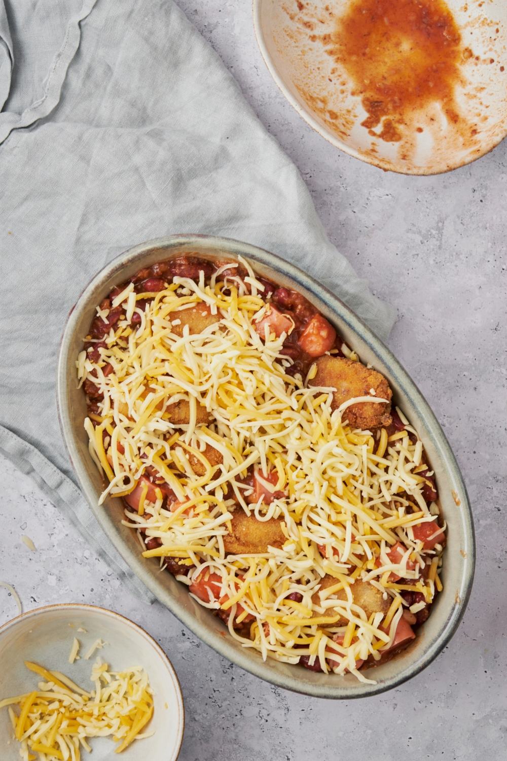 A baking dish filled with hot dog casserole covered in tater tots and shredded cheese on top.