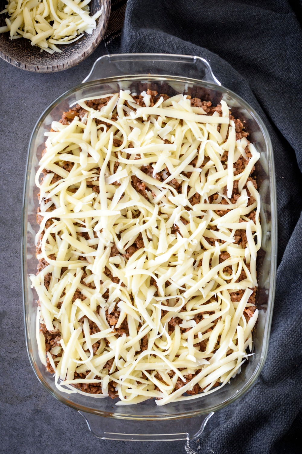 A baking dish filled with cooked and seasoned ground beef covered in shredded cheese.