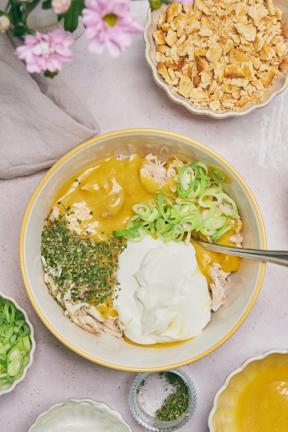 A bowl filled with shredded chicken, cream of chicken soup, sour cream, herbs, and green onion added but not combined.