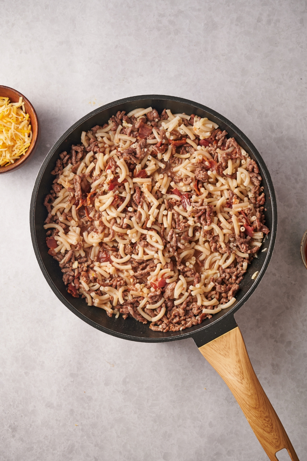 A skillet filled with cooked ground beef, bacon, and macaroni noodles.