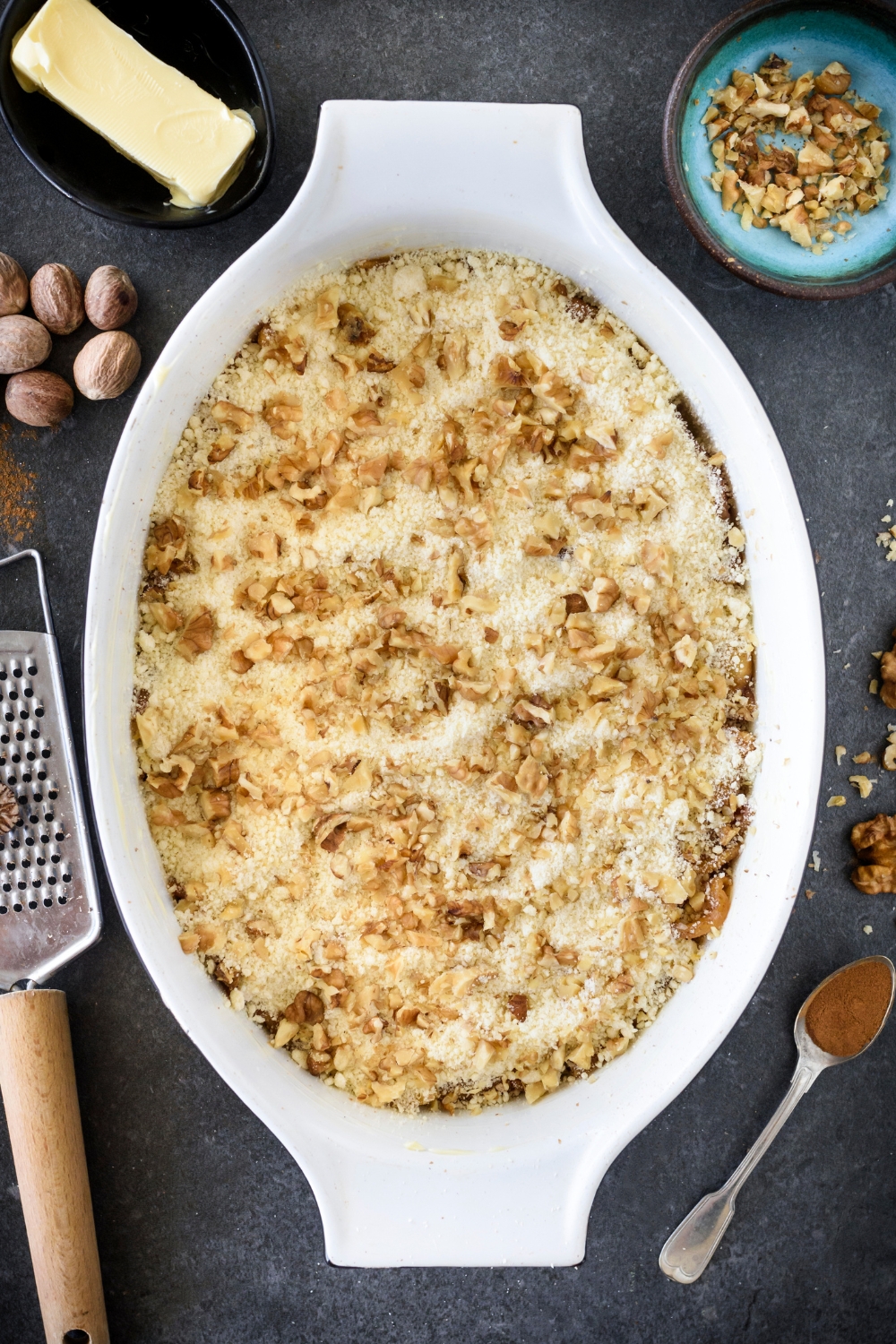 A baking dish filled with unbaked apple dump cake and topped with cake mix and chopped walnuts.