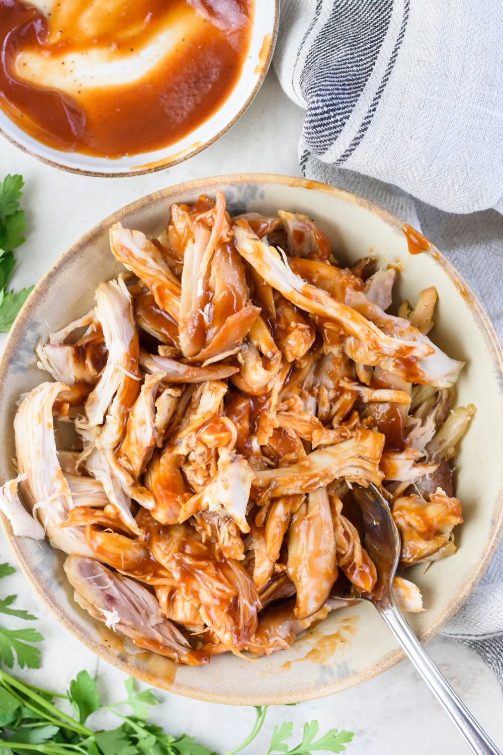 A bowl of cooked and shredded chicken mixed with barbecue sauce using a spoon that is in the bowl.