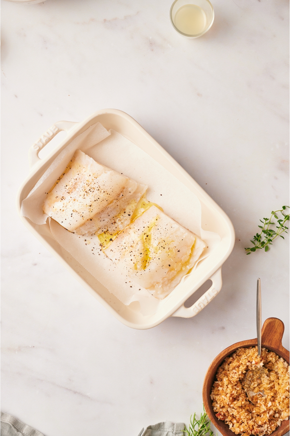 A baking dish with two cod fillets seasoned with lemon juice, salt, and pepper.