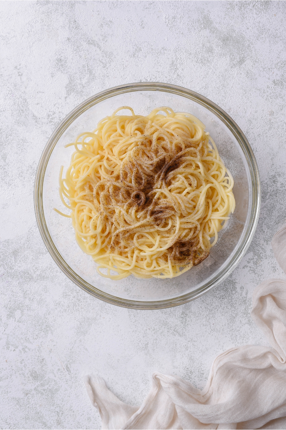 A bowl of spaghetti noodles with black pepper added but not mixed together.