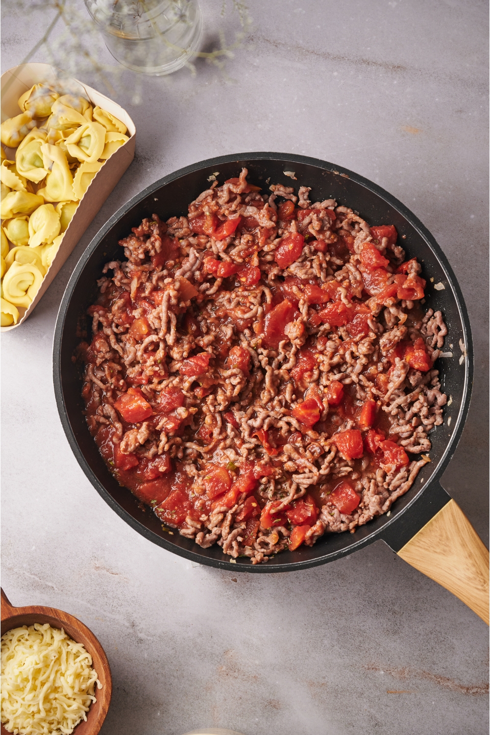 A skillet filled with cooked ground beef mixed with crushed tomatoes.