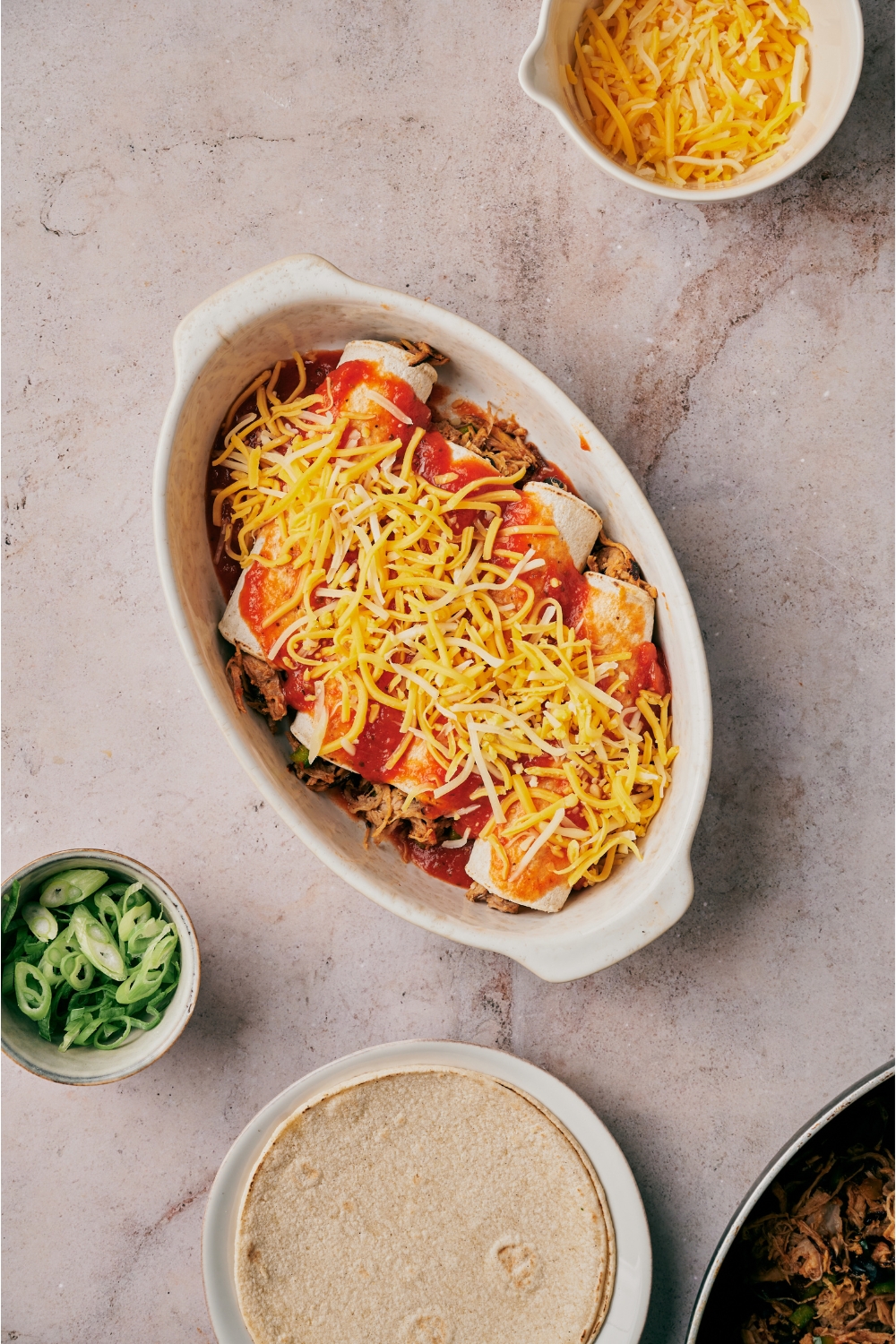 A baking dish filled with unbaked enchiladas covered in red sauce and shredded cheese.