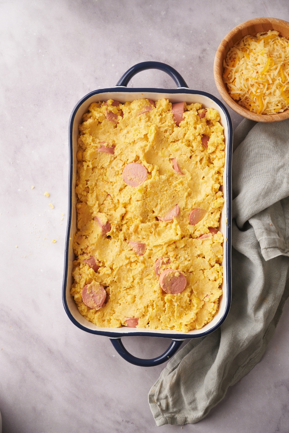 A baking dish filled with cornbread batter and hot dog slices.
