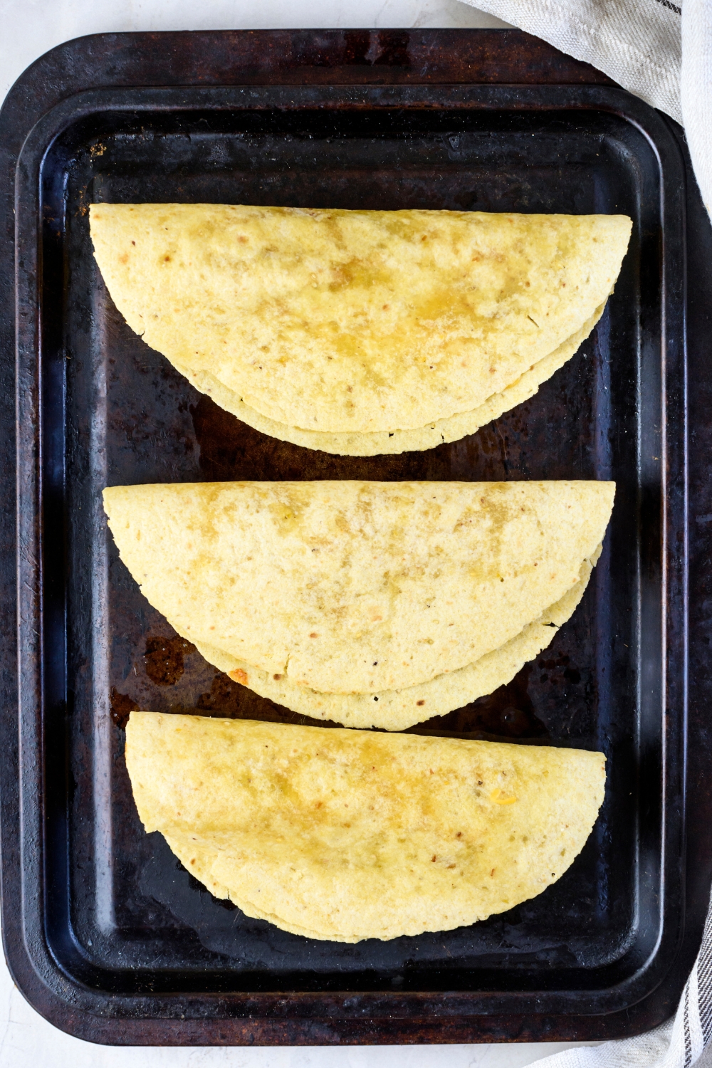 A baking sheet with three tortillas that have been baked and shaped into taco shells.
