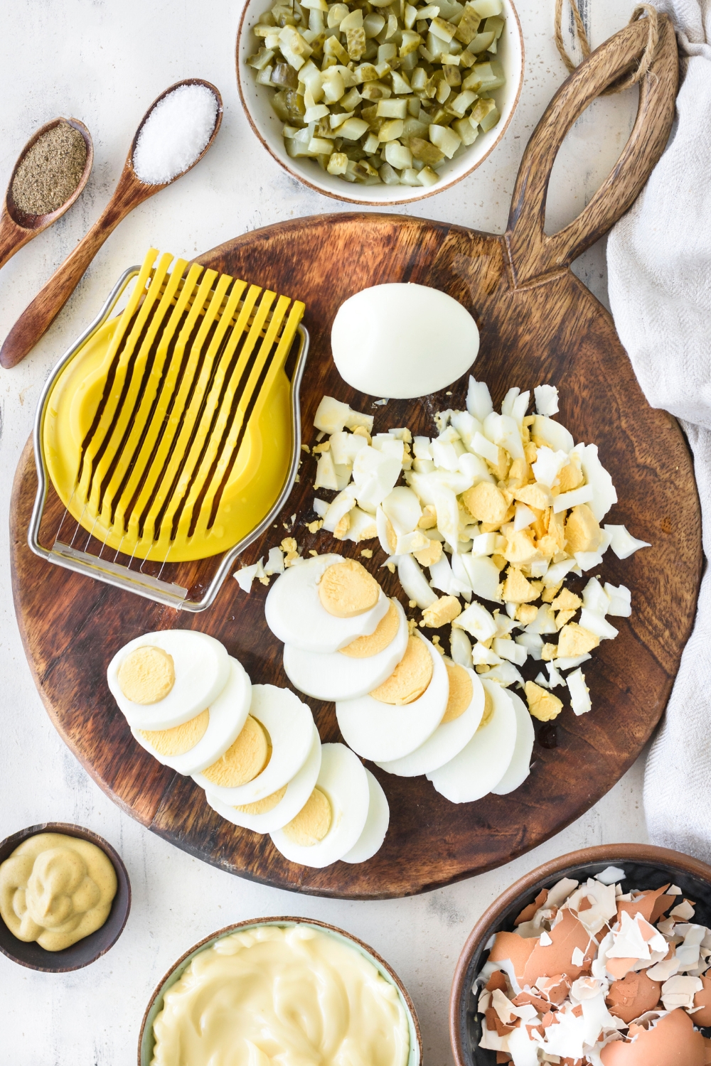 Hard-boiled eggs that have been sliced and chopped using an egg slicer that is on the wooden board next to the eggs.