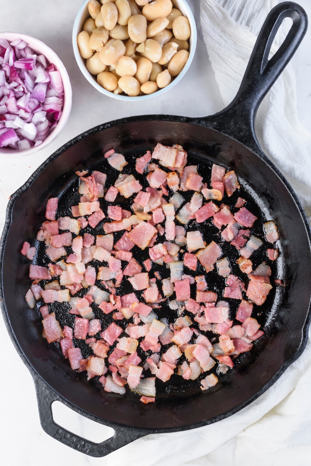 A black skillet filled with diced bacon cooking in it.