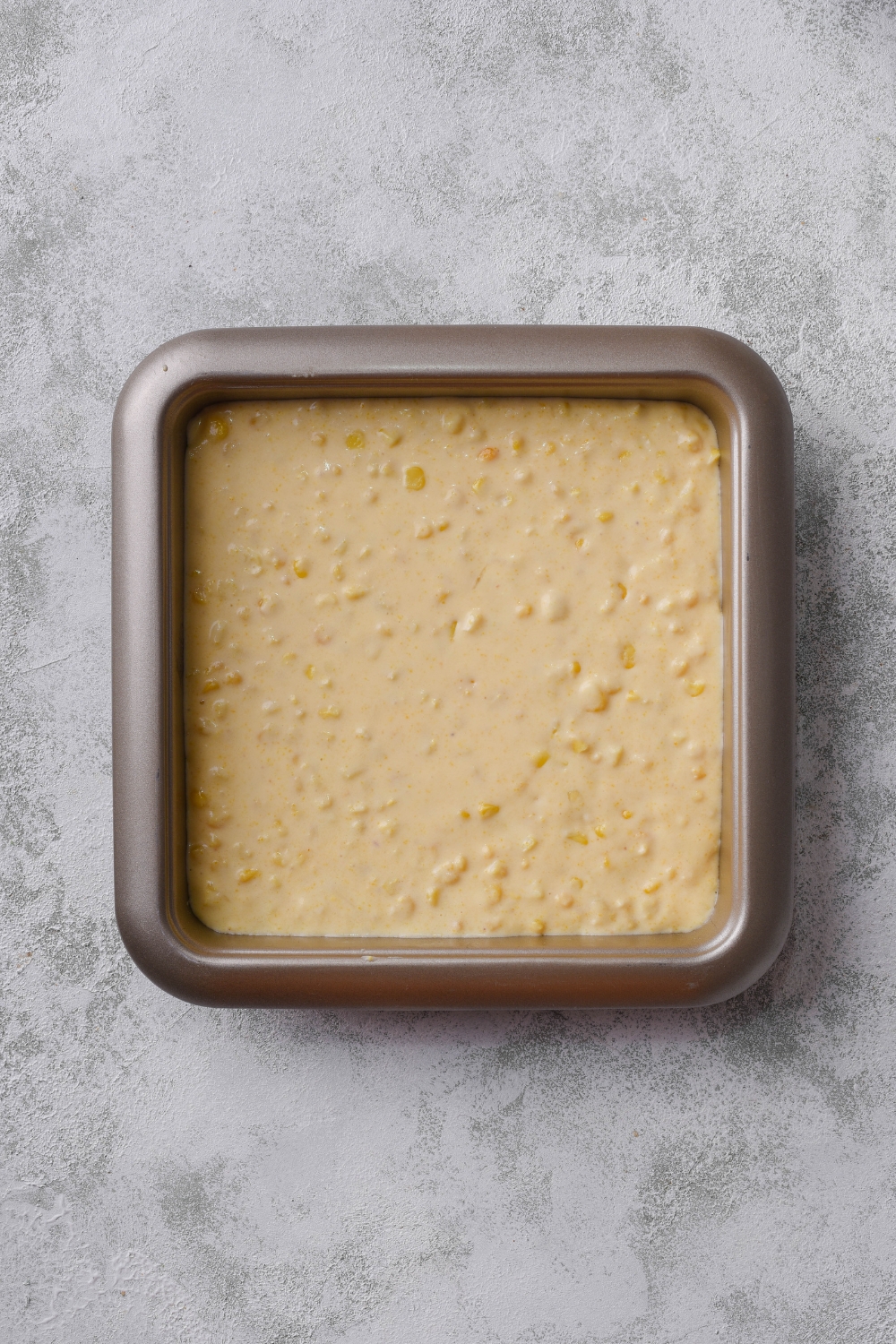 A square baking dish filled with unbaked cornbread pudding batter.