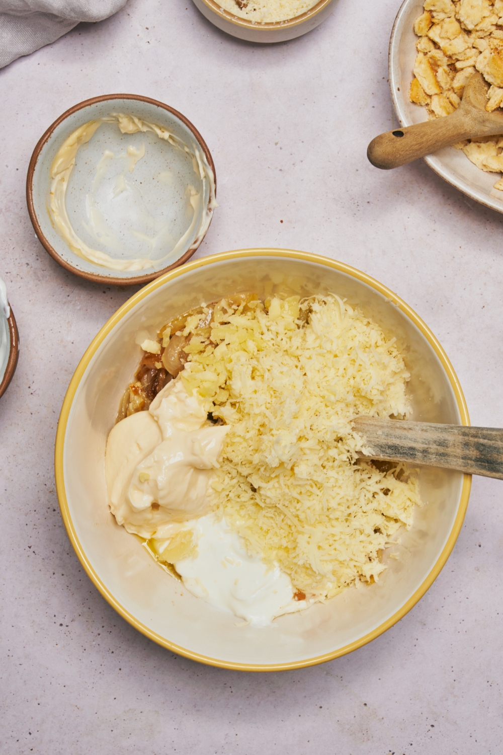 A mixing bowl filled with shredded cheese, mayonnaise, sour cream, and caramelized onion. The ingredients have not yet been mixed together.