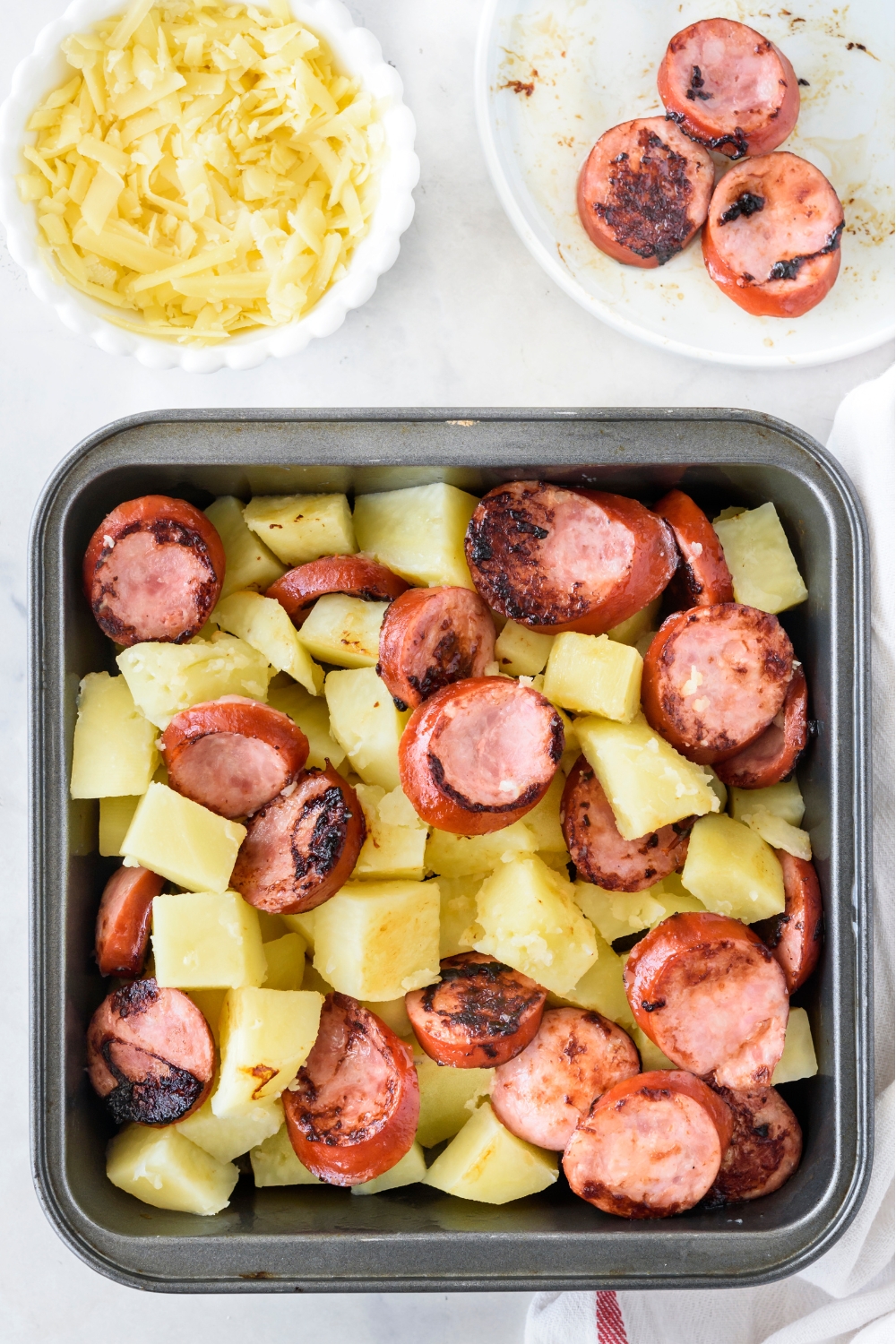 A baking dish filled with browned sausages and boiled potatoes.