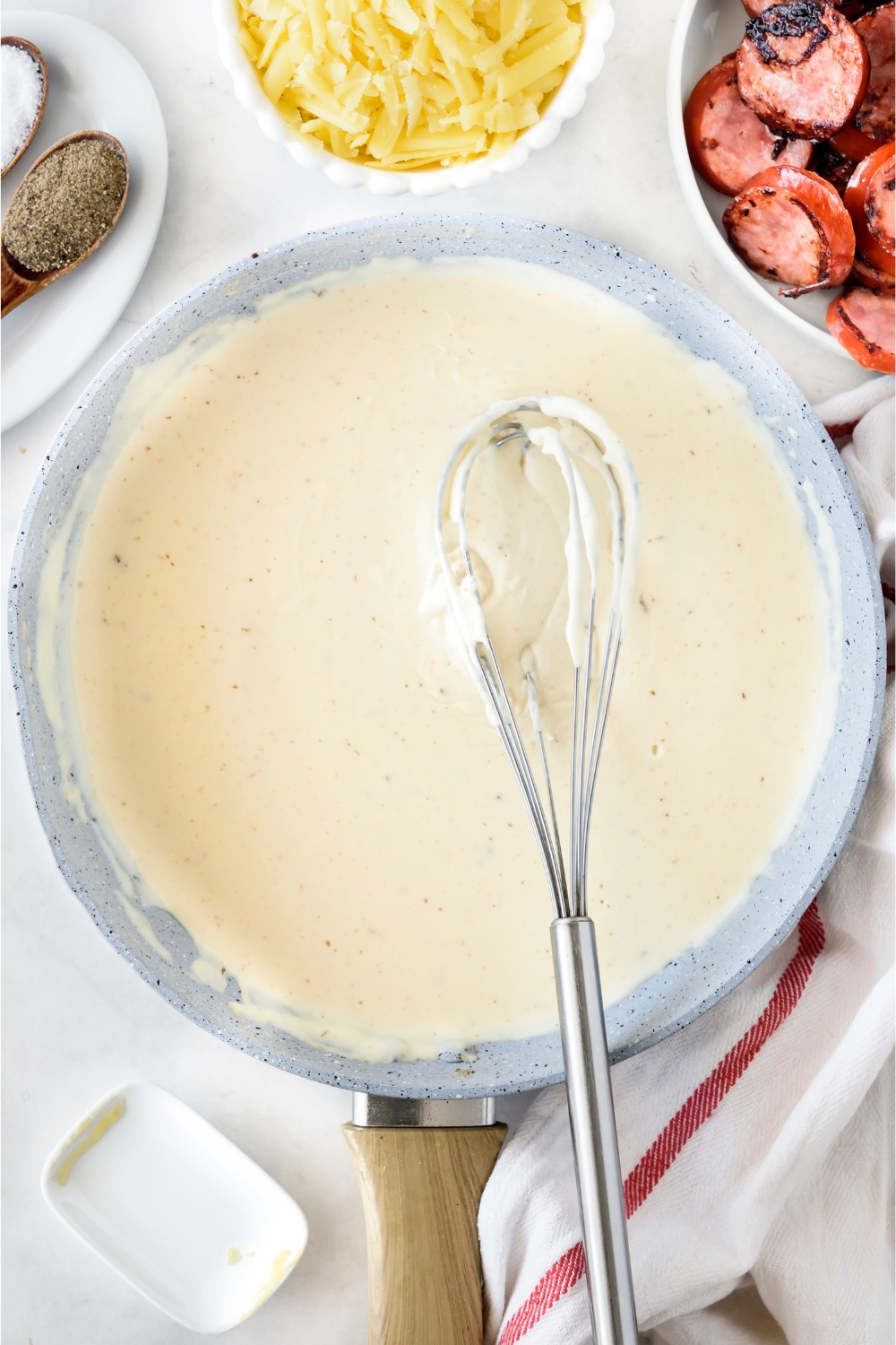 A skillet filled with cream sauce and a whisk covered in sauce is held above the skillet.