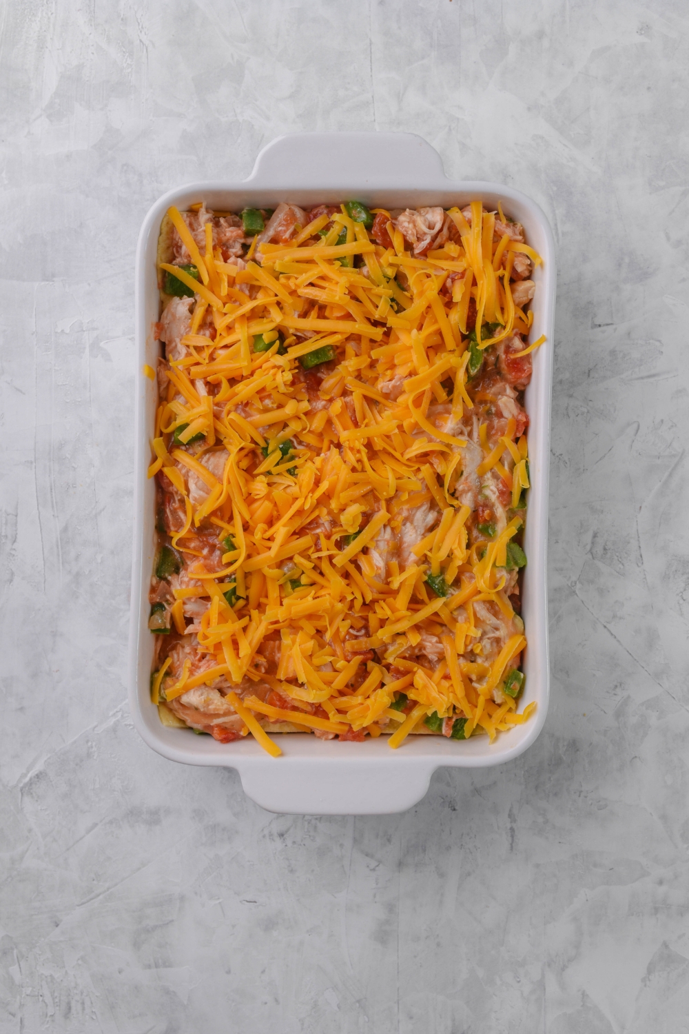 A baking dish filled with unbaked casserole covered in shredded cheese.