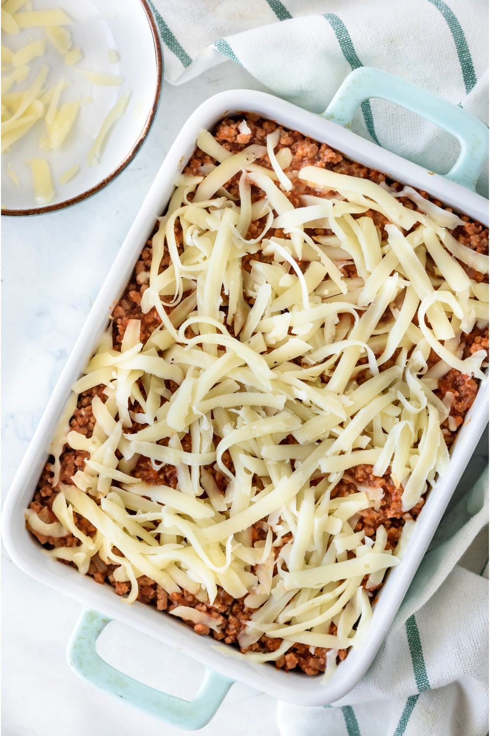 A baking dish filled with zucchini pizza casserole covered in shredded cheese.