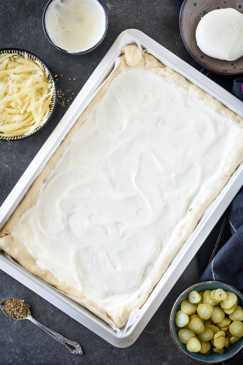 Pizza dough topped with white sauce on a baking sheet lined with parchment paper.