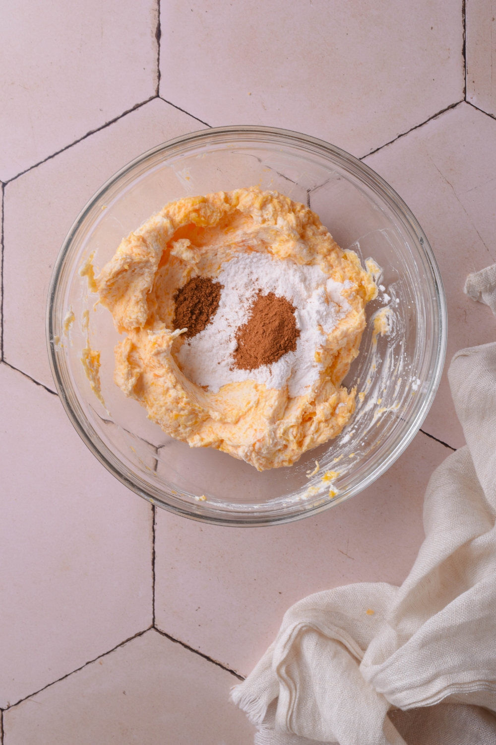 A clear bowl filled with an orange cream cheese mixture and spices have been added to the mixture but not yet combined.
