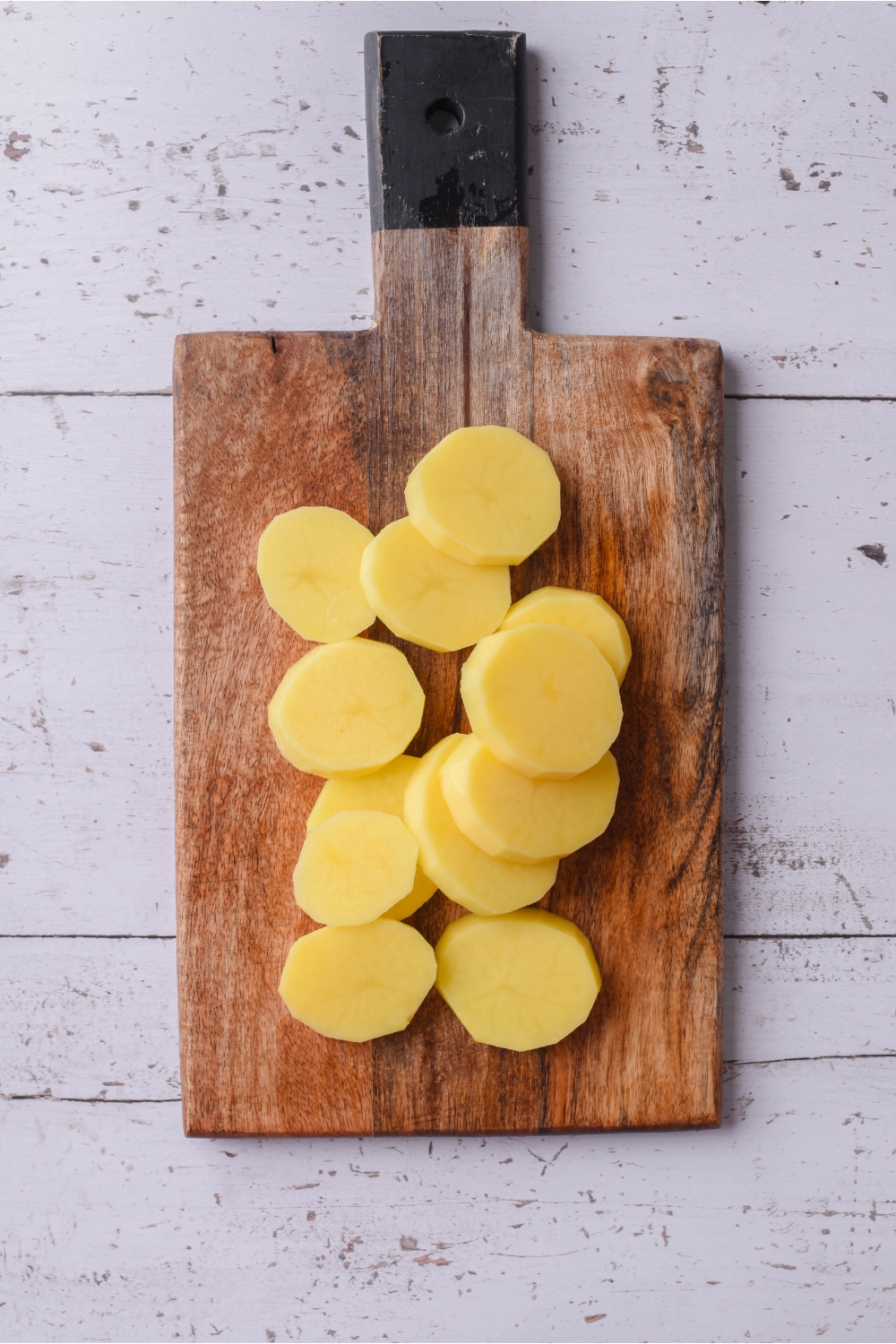 A wood cutting board with peeled and sliced potatoes piled on it.