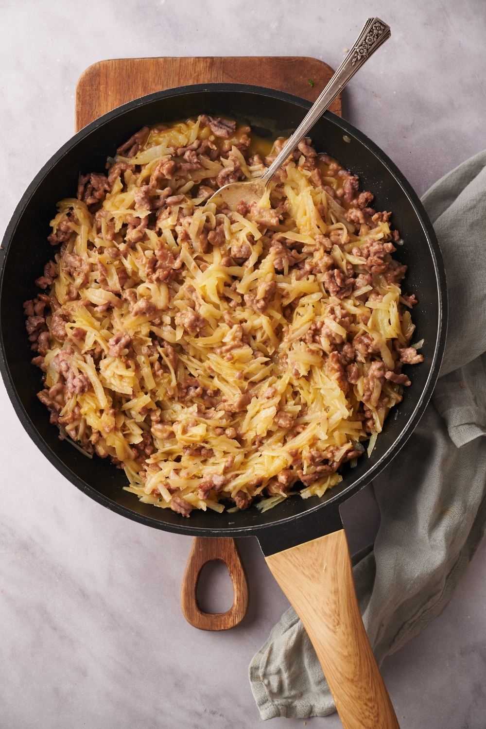 A skillet filled with cooked ground beef and hash browns in a creamy sauce mixed together with a spoon.