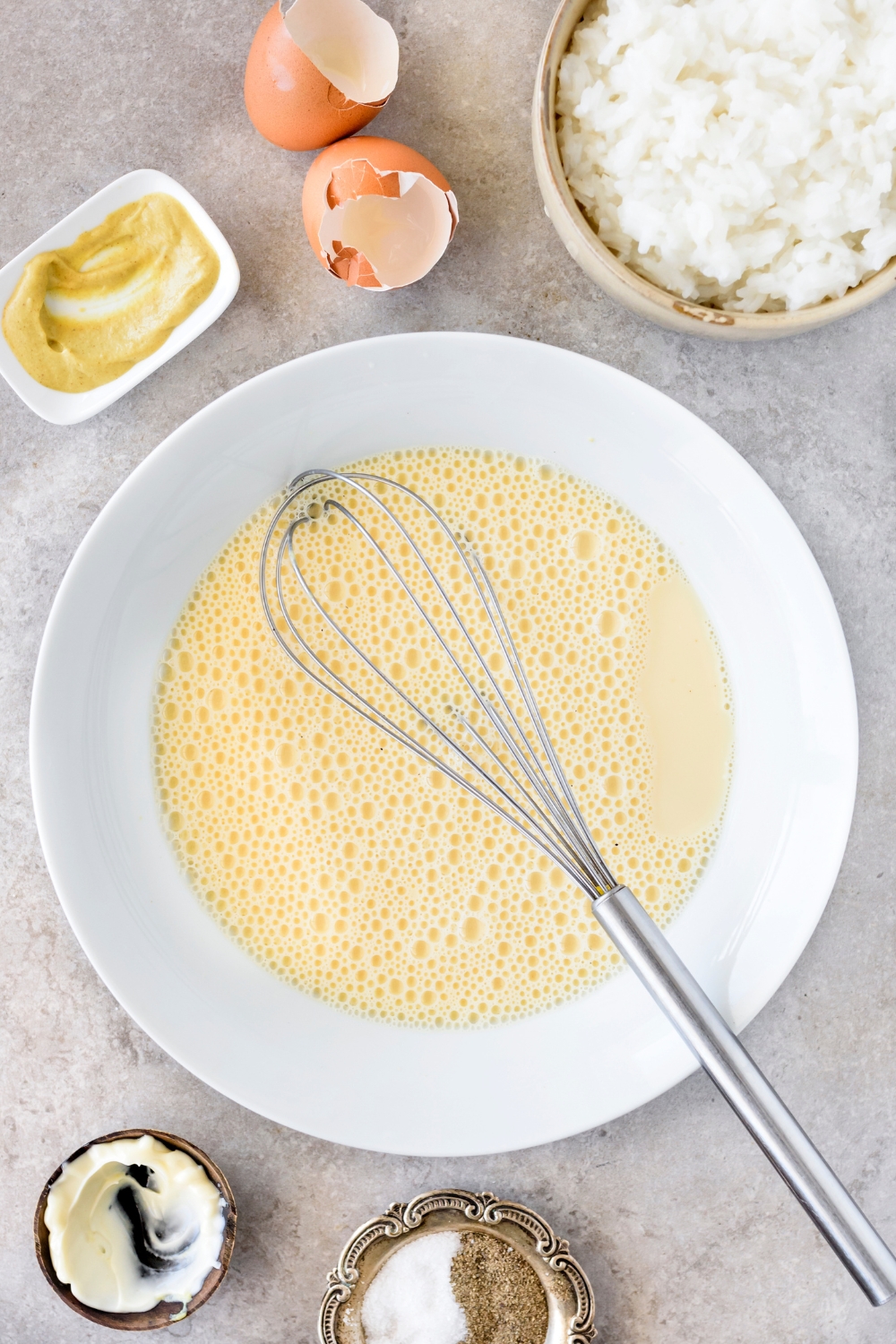 A bowl filled with a beaten egg mixture and a whisk is in the bowl.