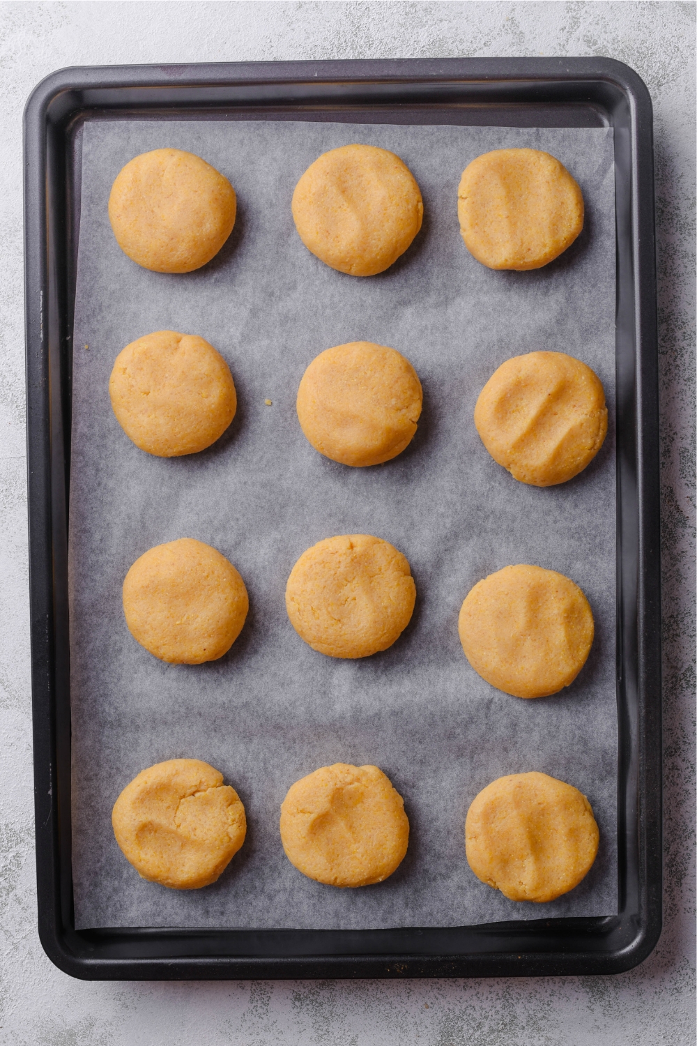One dozen unbaked cookies spaced evenly on a baking sheet lined with parchment paper.