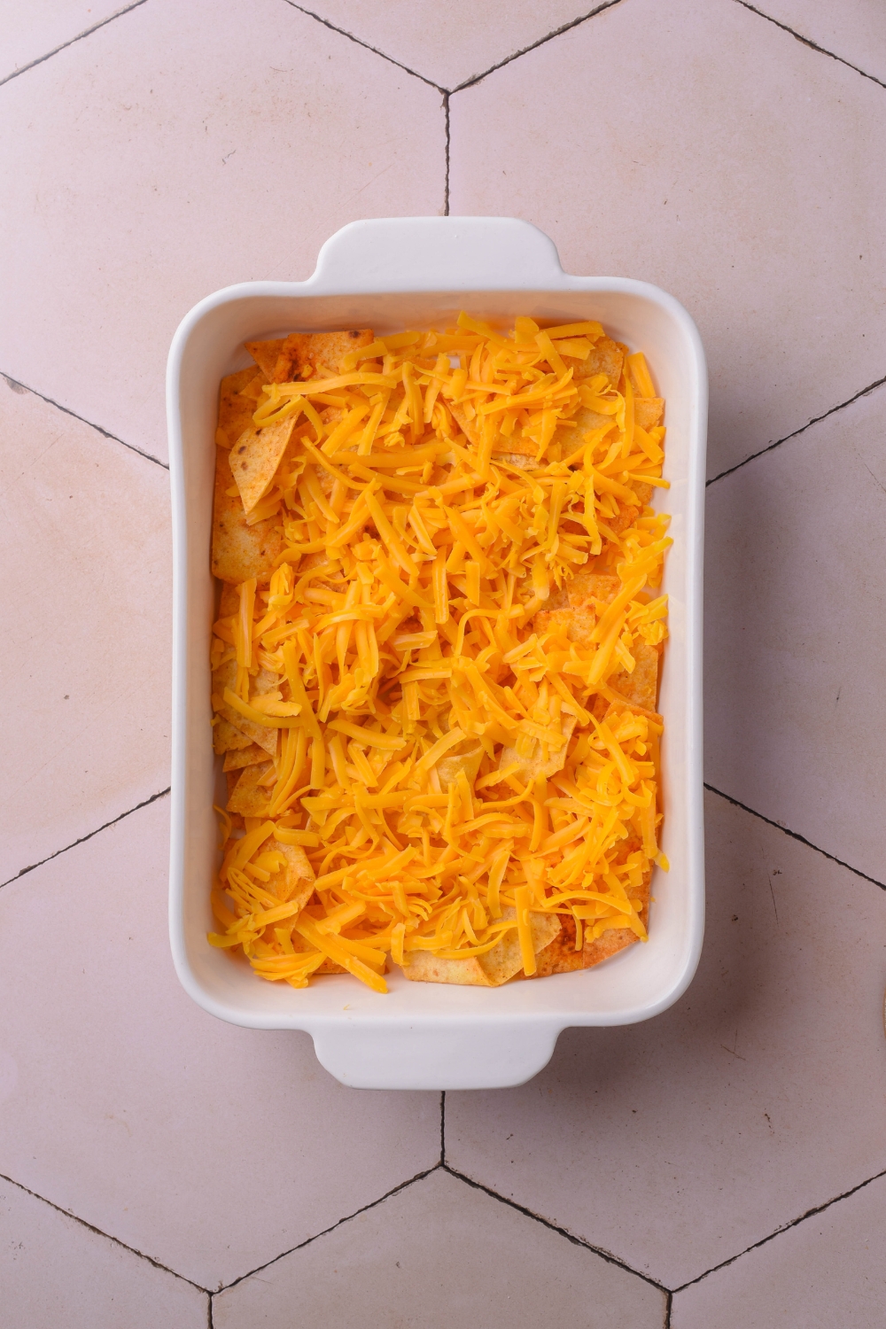 A white casserole dish filled with corn chips and shredded cheese.