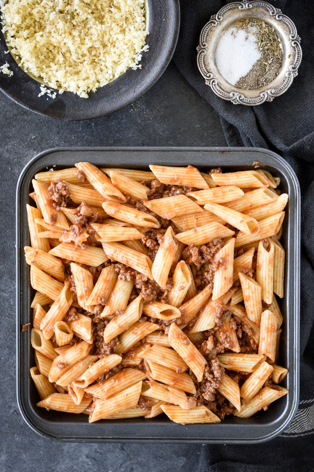 A square baking dish filled with cooked pasta and ground beef in tomato sauce.
