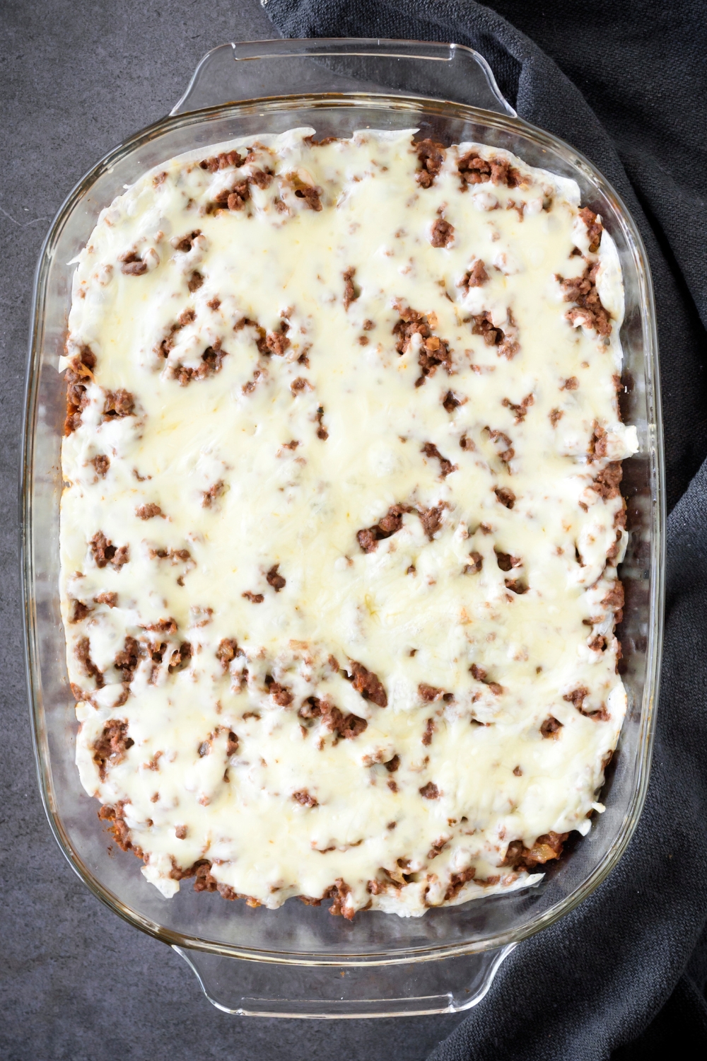 A baking dish filled with cooked and seasoned ground beef covered in melted cheese.