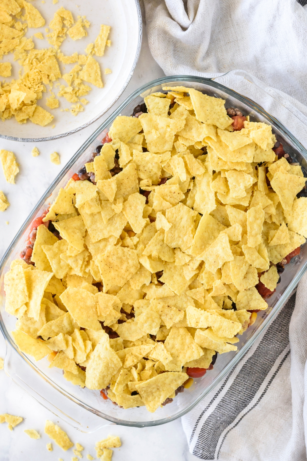 A clear baking dish filled with unbaked casserole covered in crushed tortilla chips.