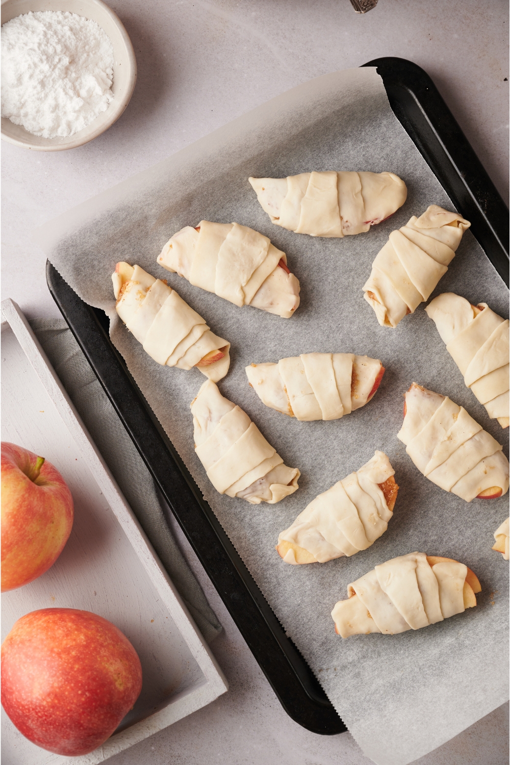 Unbaked apple turnovers wrapped in crescent roll dough on a baking sheet lined with parchment paper.