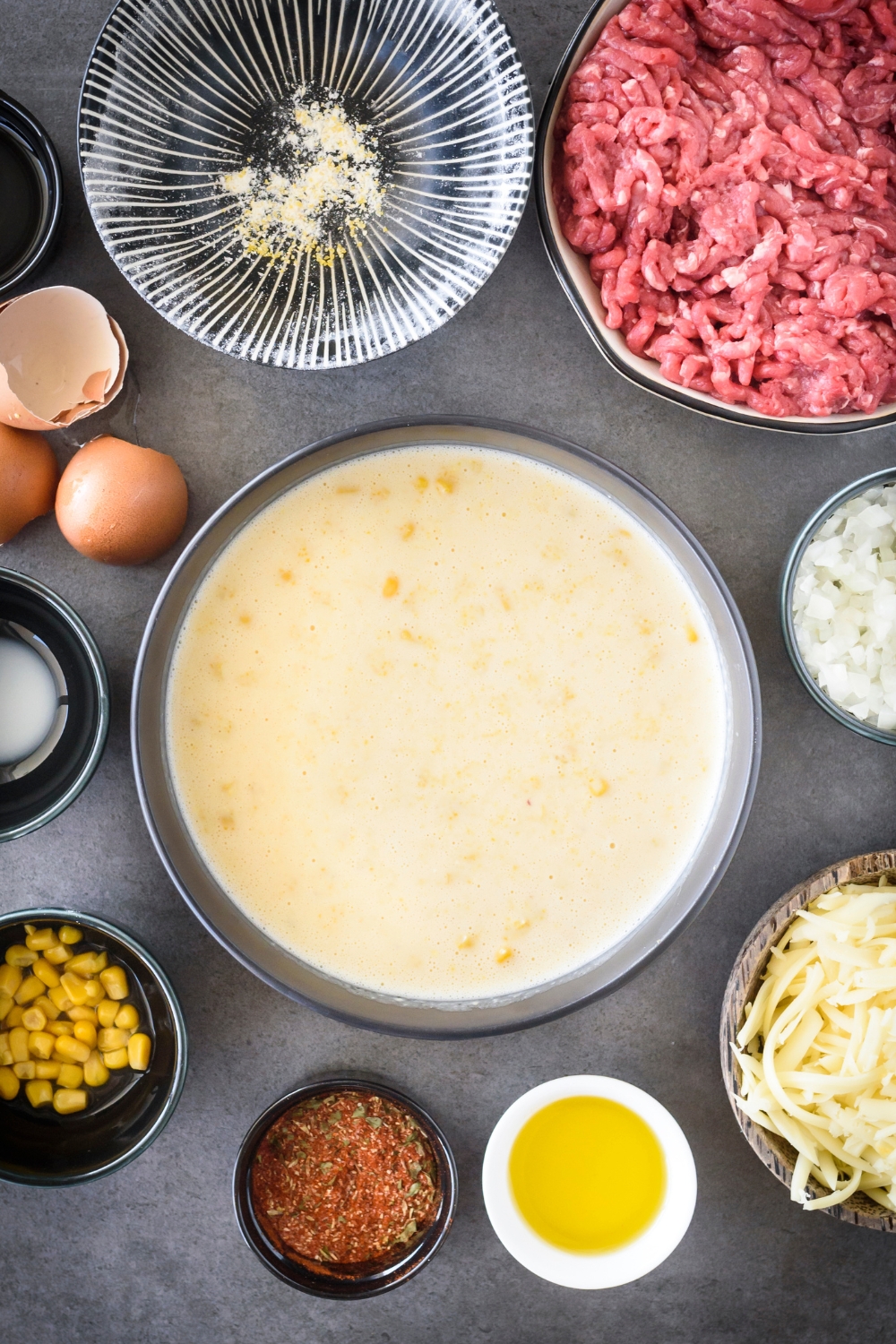 A bowl filled with cornbread batter surrounded by an assortment of ingredients.